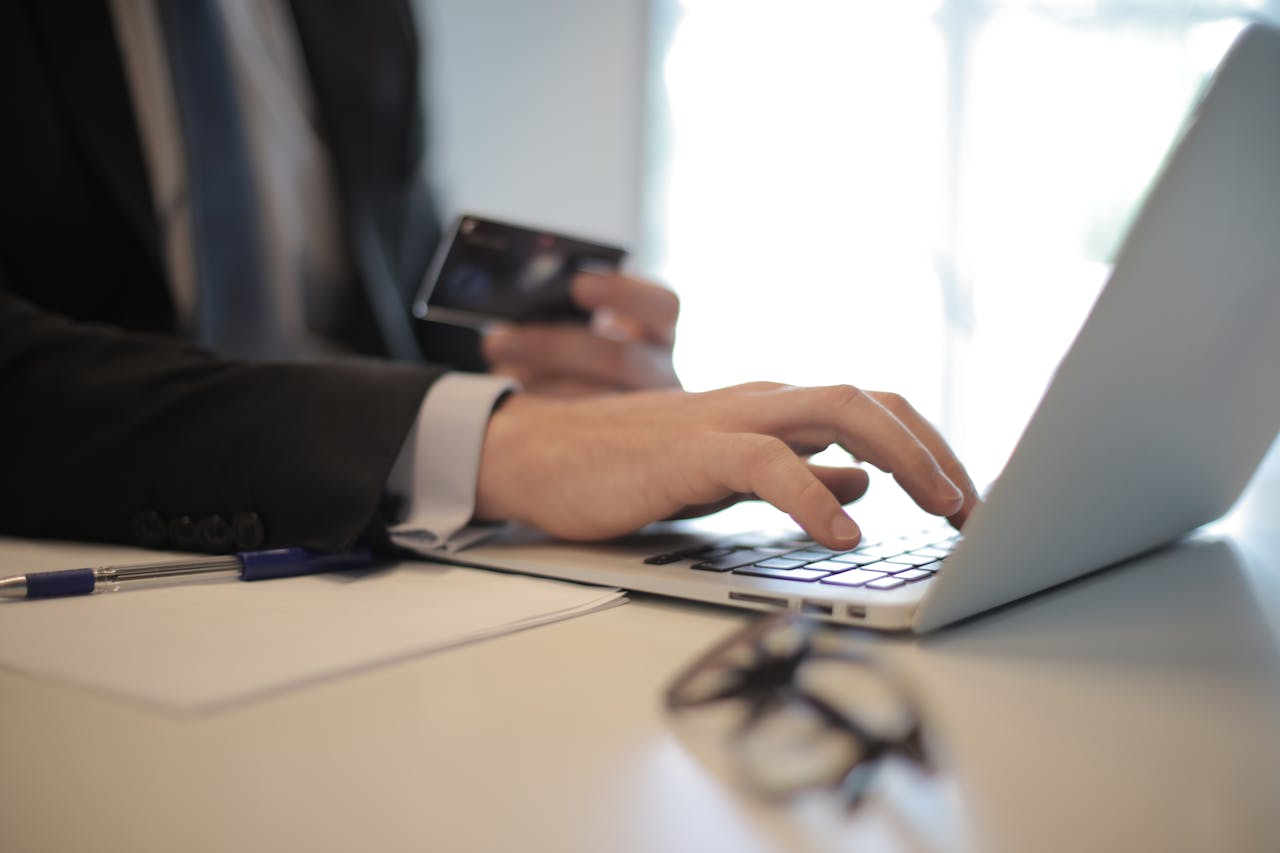 Man in suit using laptop and credit card for online transaction at work.